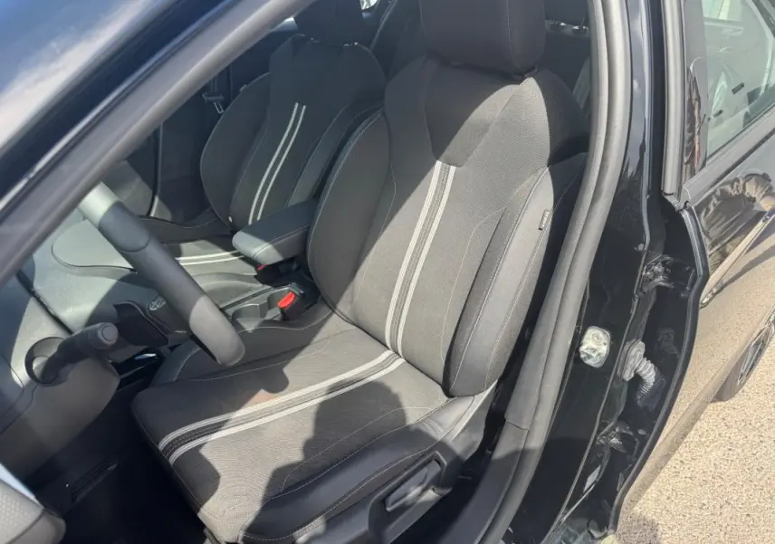 Vue intérieure côté conducteur d'une Opel Corsa noire 2025, sièges tissu noir avec bandes grises et accoudoir central.