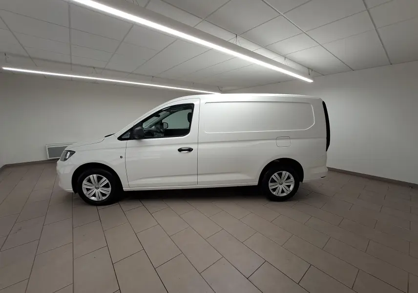 Vue de profil côté gauche d’un Volkswagen Caddy Cargo Maxi blanc Candy 2026 dans un intérieur neutre.