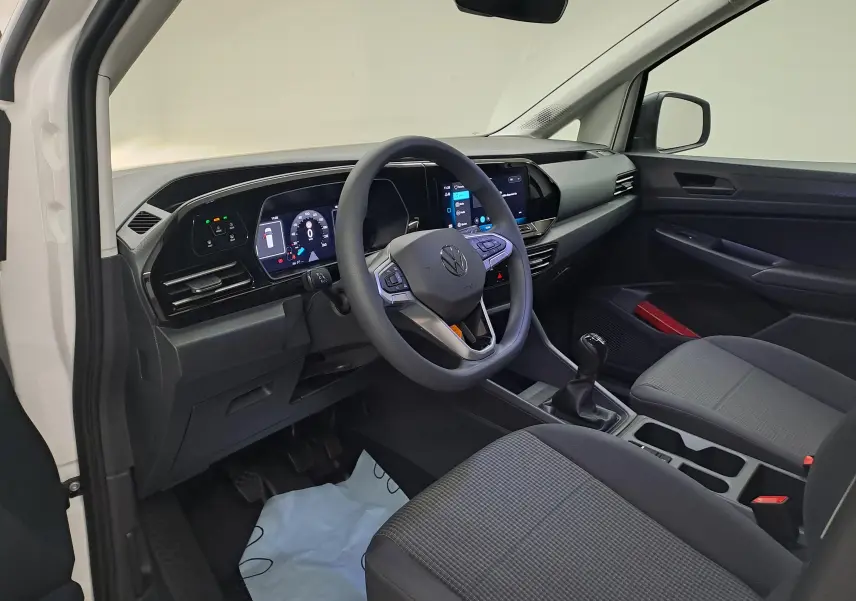 Vue intérieure côté conducteur du Volkswagen Caddy Cargo Maxi blanc Candy 2026, avec tableau de bord numérique et boîte manuelle.