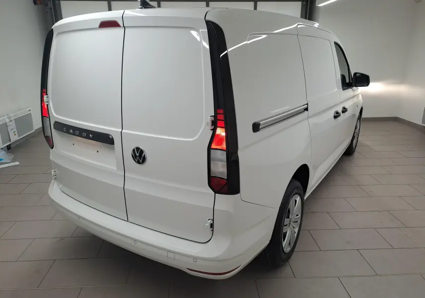 Vue 3/4 arrière droite d’un Volkswagen Caddy Cargo Maxi blanc Candy avec feux arrière allumés dans un intérieur.