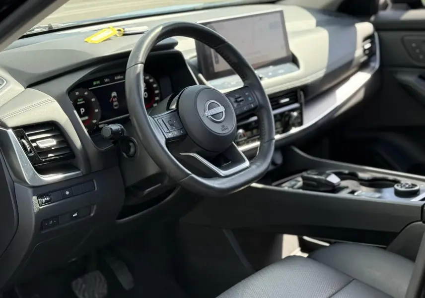 Vue intérieure côté conducteur du Nissan X-TRAIL 2024, volant cuir noir et tableau de bord digital avec écran tactile.