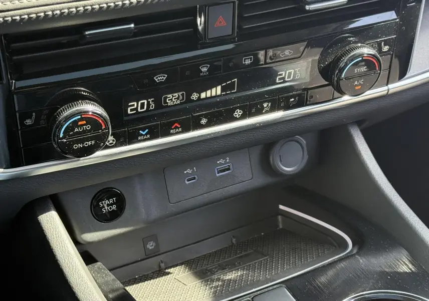 Vue rapprochée du tableau de bord noir du Nissan X-TRAIL 2024, montrant la climatisation automatique bi-zone et les ports USB.