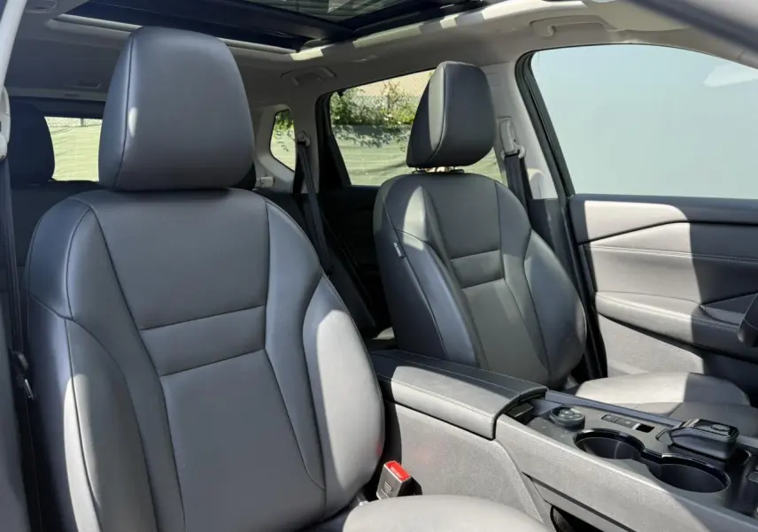 Intérieur Nissan X-TRAIL 2024 vu côté droit, sièges cuir noirs et toit panoramique en verre ouvert.
