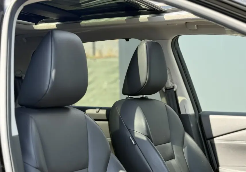 Gros plan sur les sièges avant en cuir noir du Nissan X-TRAIL 2024 avec toit panoramique visible depuis la portière ouverte.