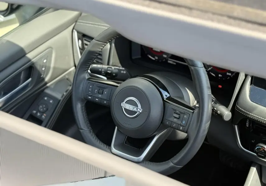 Vue rapprochée du volant cuir noir du Nissan X-TRAIL 2024 avec commandes intégrées et tableau de bord digital.