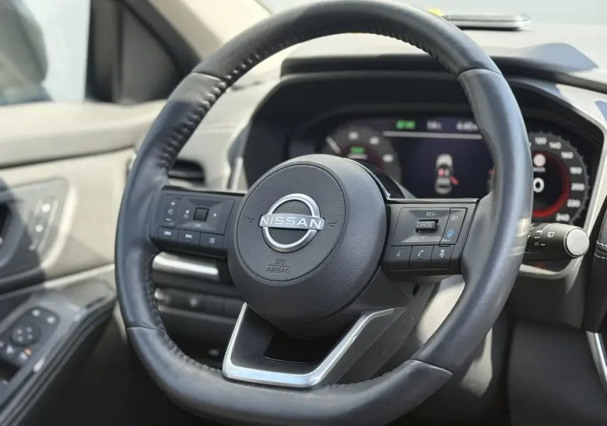 Vue rapprochée du volant en cuir noir du Nissan X-TRAIL 2024 avec commandes intégrées et tableau de bord digital.