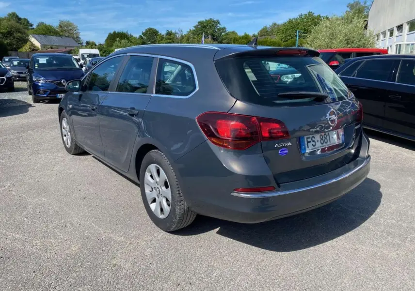 Opel Astra Sports Tourer gris vue 3/4 arrière droit, avec feux arrière rouges et toit avec antenne shark fin.