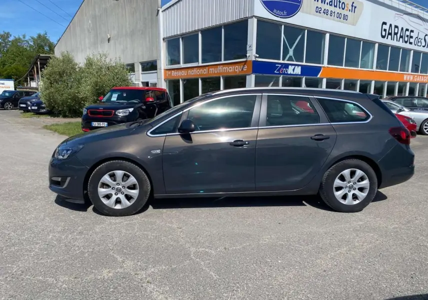 Opel Astra Sports Tourer gris vue de profil côté gauche, garée devant un garage multimarque.
