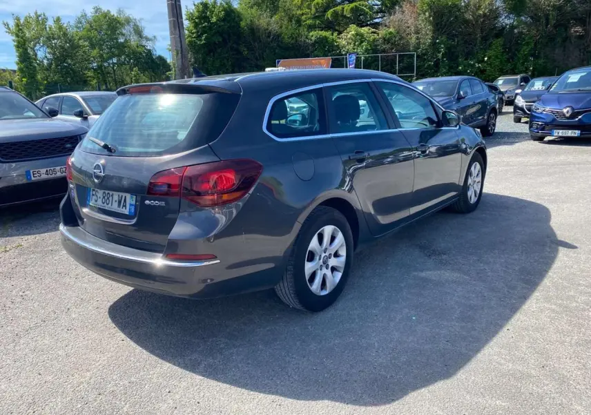Opel Astra Sports Tourer gris vue 3/4 arrière droit, avec feux arrière rouges et jantes blanches.
