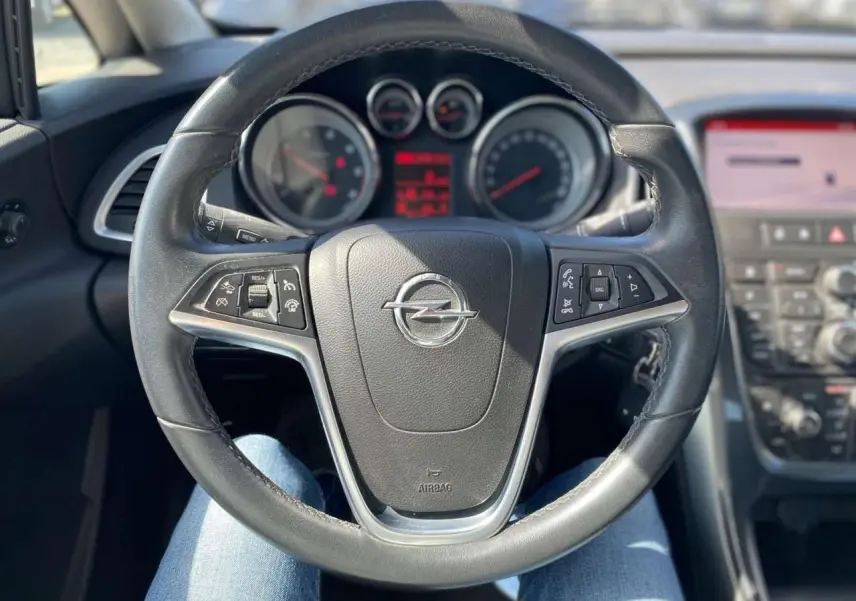 Vue intérieure centrée sur le volant noir de l’Opel Astra Sports Tourer 2014 avec commandes intégrées au tableau de bord.
