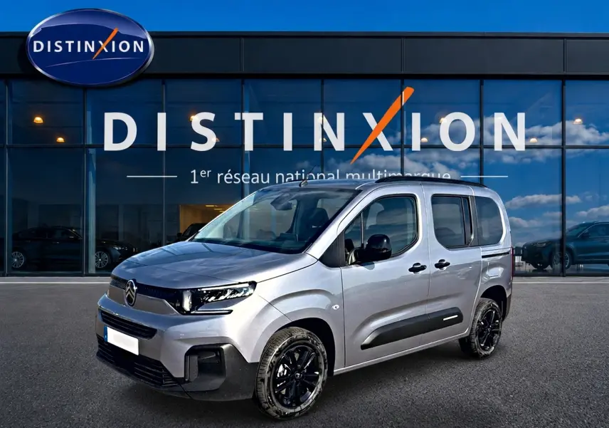 Citroën Berlingo Steel Grey en 3/4 avant droit, avec jantes noires et barres de toit visibles devant un bâtiment Distinxion.