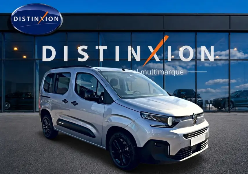 Vue 3/4 avant droit du Citroën Berlingo 2026 gris acier avec barres de toit et jantes noires devant un showroom Distinxion.