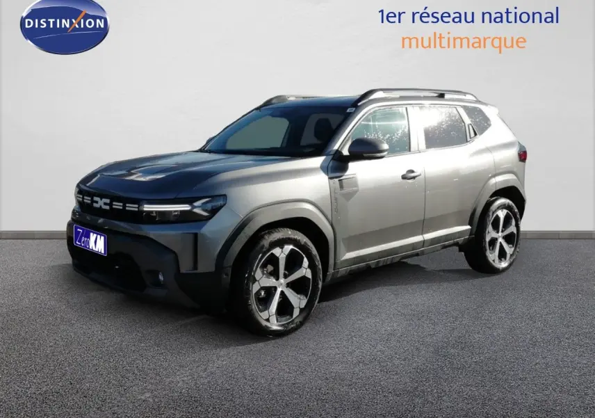 Dacia Duster gris schiste métal en 3/4 avant droit, avec jantes alliage bicolores et barres de toit visibles.