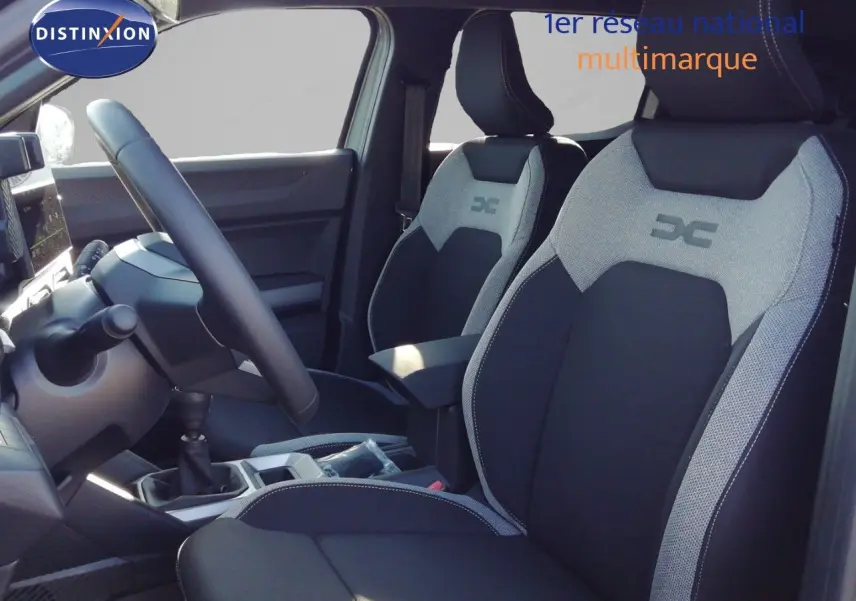 Vue intérieure côté conducteur du Dacia Duster 2026, sièges tissu noir et gris avec logo DC brodé.