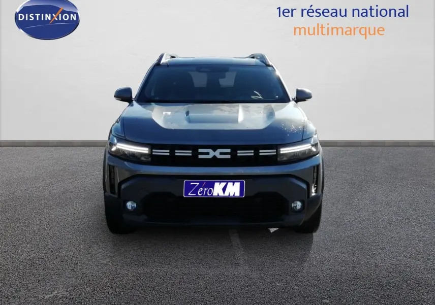 Vue frontale du Dacia Duster TCE MHEV 140ch Journey gris schiste métal avec calandre distinctive et feux LED allumés.