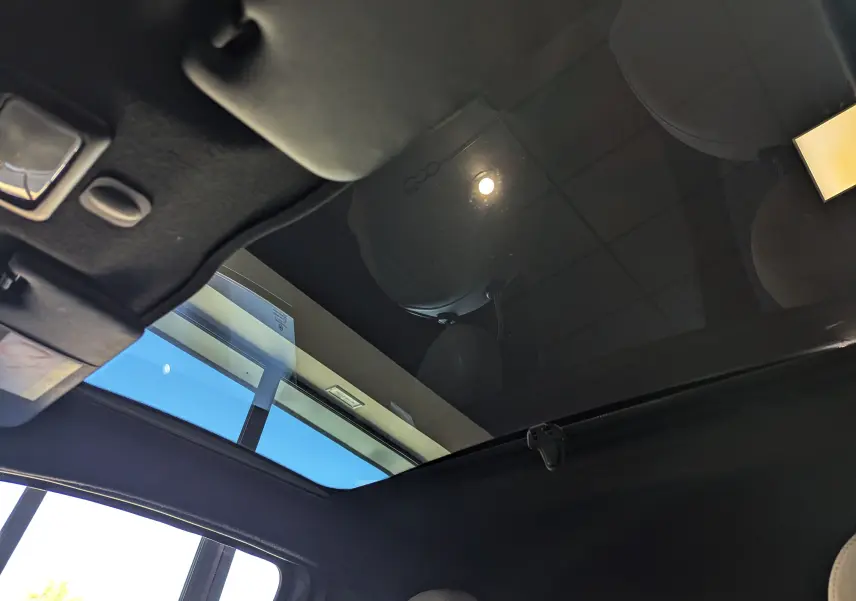 Toit panoramique en verre du Fiat 500 1.0 70 CH Hybride DolceVita, vue intérieure vers le ciel et plafond noir.