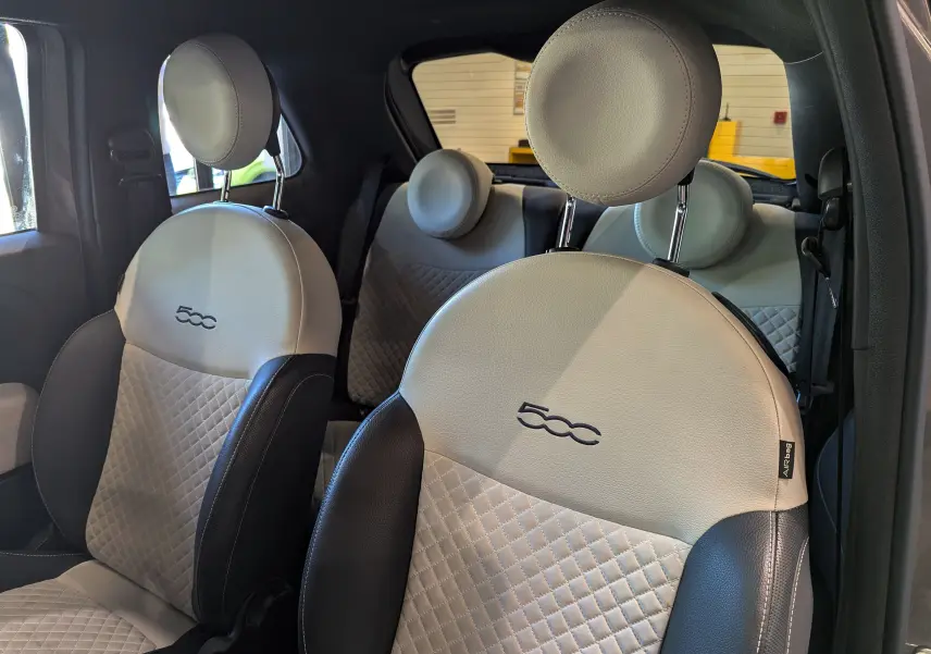 Intérieur de la FIAT 500 1.0 hybride, vue côté droit sur sièges avant en cuir beige et noir avec logo 500 brodé.