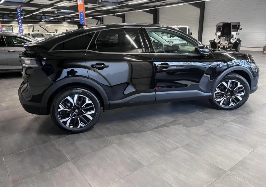 Profil droit d'une Citroën C4 2025 noir métal avec jantes alliage 18'' AMBER diamantées en intérieur showroom.