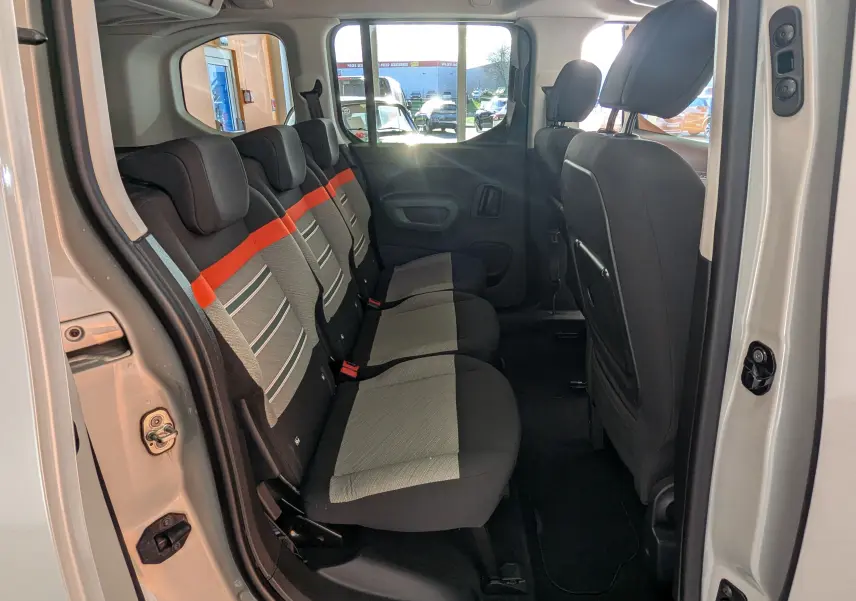 Vue latérale intérieure montrant la banquette arrière grise avec bande orange du Citroën Berlingo beige 2019, portes ouvertes.