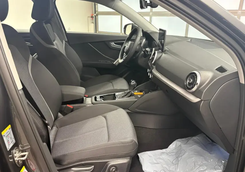 Intérieur avant droit de l’Audi Q2 35 TFSI 150 S tronic 7 S line avec sièges tissu gris et tableau de bord noir.