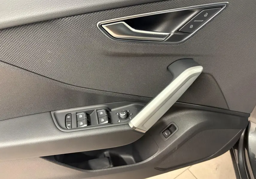 Gros plan sur la porte avant gauche de l’Audi Q2 gris Daytona, montrant les commandes de vitres et la poignée intérieure argentée.