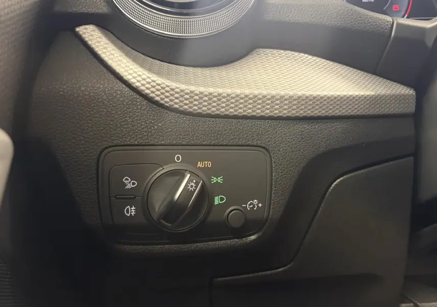Gros plan sur le bouton de commande des phares à gauche du tableau de bord de l'Audi Q2 35 TFSI S Line 2026.
