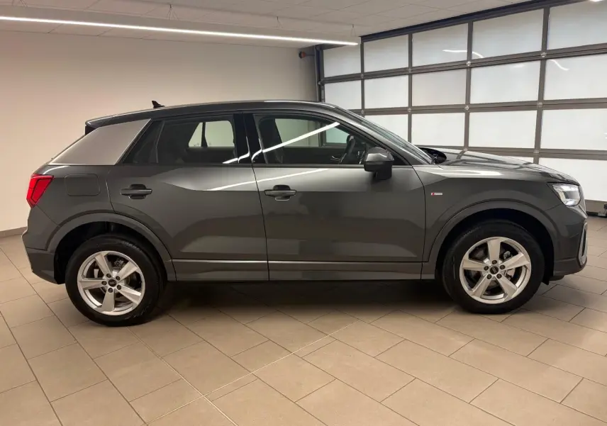 Audi Q2 35 TFSI S Line gris Daytona vue de profil côté gauche en intérieur, avec jantes alliage et toit noir.