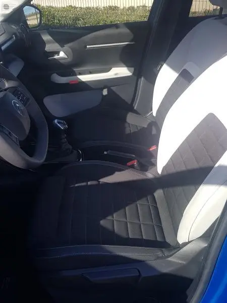 Vue intérieure côté conducteur de la Citroën C3 bleu foncé 2024, sièges bicolores noir et blanc, volant et levier de vitesse visibles.