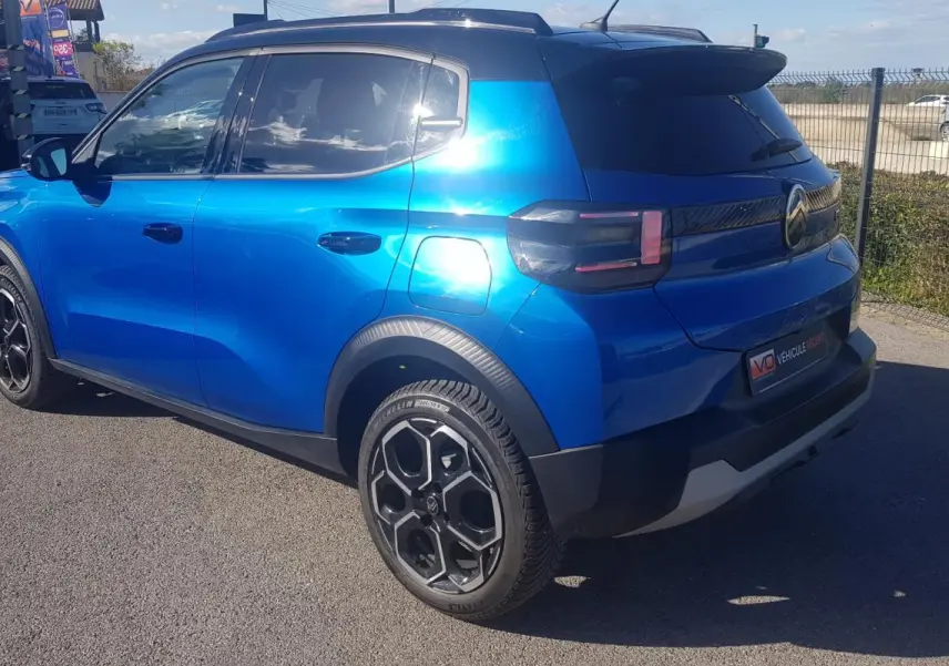 Vue 3/4 arrière droite d'une Citroën C3 bleu foncé 2024 avec jantes alliage noires et barres de toit.