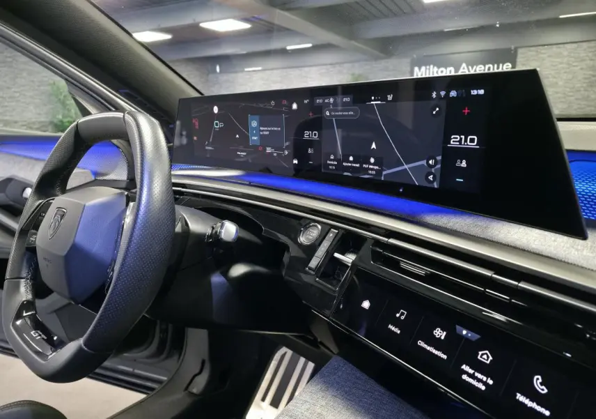 Vue intérieure du tableau de bord et volant cuir noir laqué du Peugeot 3008 gris avec écran panoramique 21 pouces affichant la navigation.