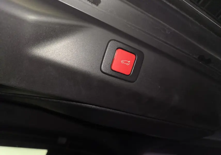 Bouton rouge de fermeture électrique du hayon sur le bord intérieur du coffre du Peugeot 3008 gris 2025.