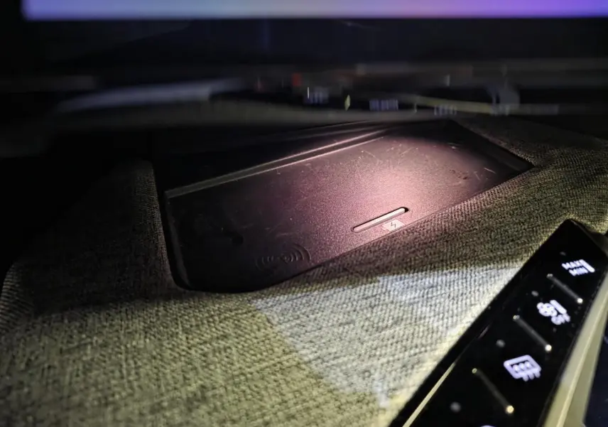 Détail du chargeur sans fil intégré dans la console centrale tissu gris du Peugeot 3008 hybride 2025.