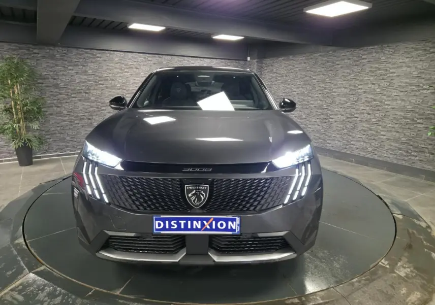 Vue frontale d'un Peugeot 3008 gris métallisé 2025 avec calandre noire et feux LED à griffes distinctifs allumés.