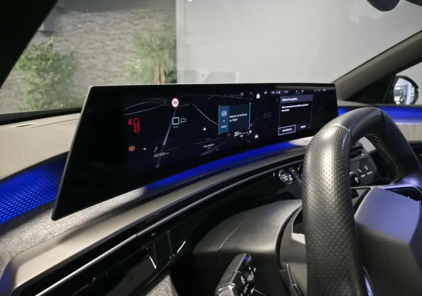 Vue intérieure du tableau de bord numérique panoramique et volant perforé du Peugeot 3008 gris hybride 2025.