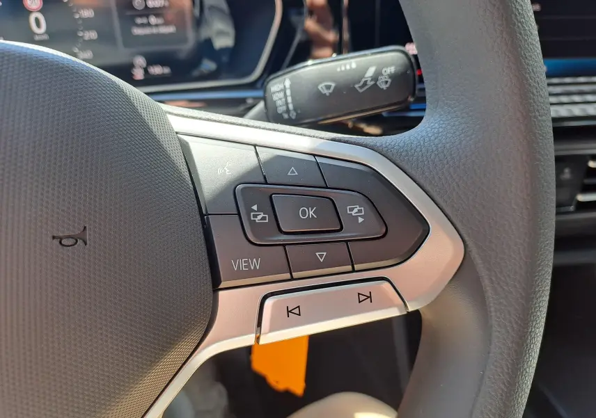 Gros plan sur les commandes au volant côté gauche du Volkswagen Caddy Cargo Maxi blanc, avec boutons multifonctions et tableau de bord partiel.