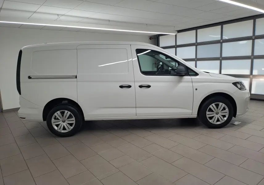 Vue de profil côté droit d'un Volkswagen Caddy Cargo Maxi blanc Candy 2026 en intérieur, avec portes latérales coulissantes.