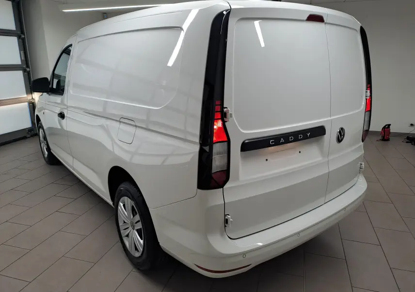 Vue 3/4 arrière droite d’un Volkswagen Caddy Cargo Maxi blanc Candy avec feux arrière allumés en intérieur.