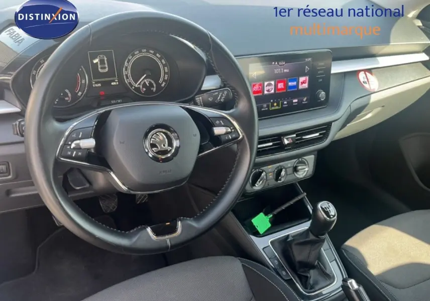 Vue intérieure de face du poste de conduite d'une Skoda Fabia blanche, avec volant cuir multifonction et écran tactile central.