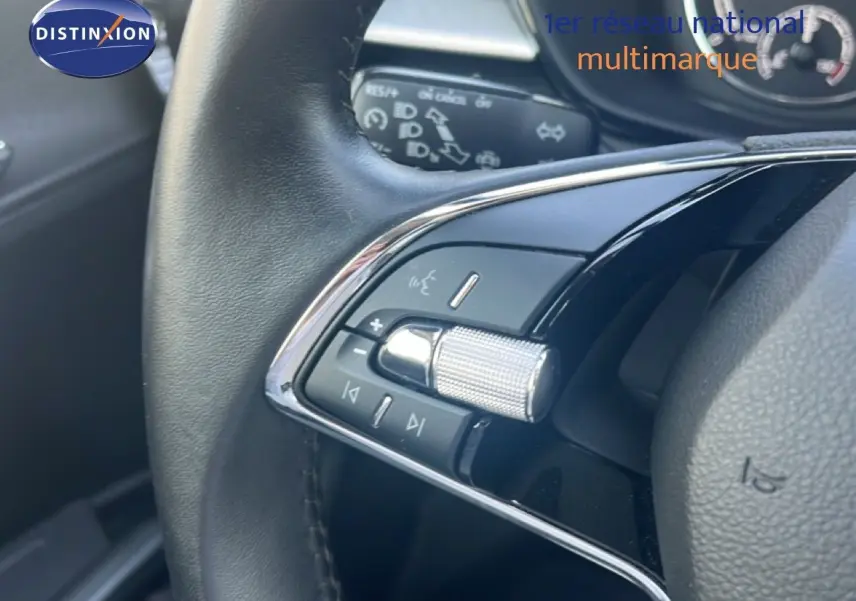 Gros plan sur les commandes multifonctions en chrome et noir du volant d'une Skoda Fabia blanche, intérieur noir.