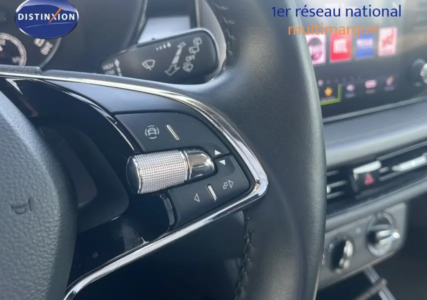Gros plan sur la commande multifonction du volant noir d’une Skoda Fabia blanche, avec tableau de bord et écran tactile en arrière-plan.