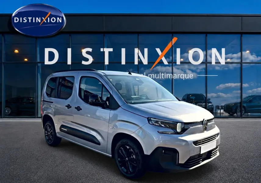 Vue 3/4 avant droite du Citroën Berlingo Steel Grey avec barres de toit et jantes noires devant showroom Distinxion.