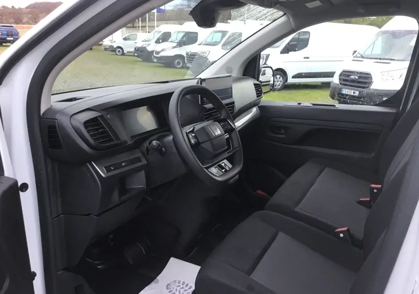 Vue intérieure côté conducteur du Fiat Scudo Fourgon blanc 2024, montrant le tableau de bord moderne et les sièges noirs.