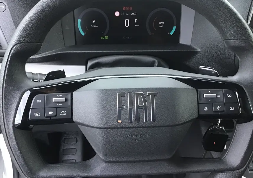 Volant noir avec logo FIAT en gros plan, tableau de bord digital affichant vitesse et compte-tours du fourgon blanc FIAT Scudo 2024.