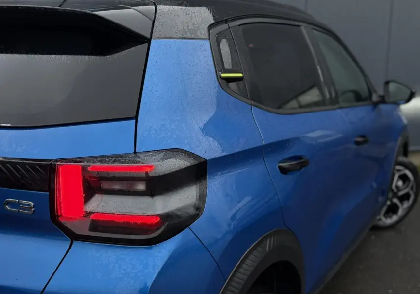 Vue 3/4 arrière droite d'une Citroën C3 2025 Bright Blue avec toit noir Perla et feux arrière LED 3D allumés.