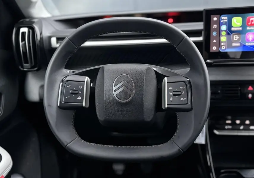 Vue rapprochée du volant noir de la Citroën C3 2025 avec commandes intégrées et écran tactile en arrière-plan.