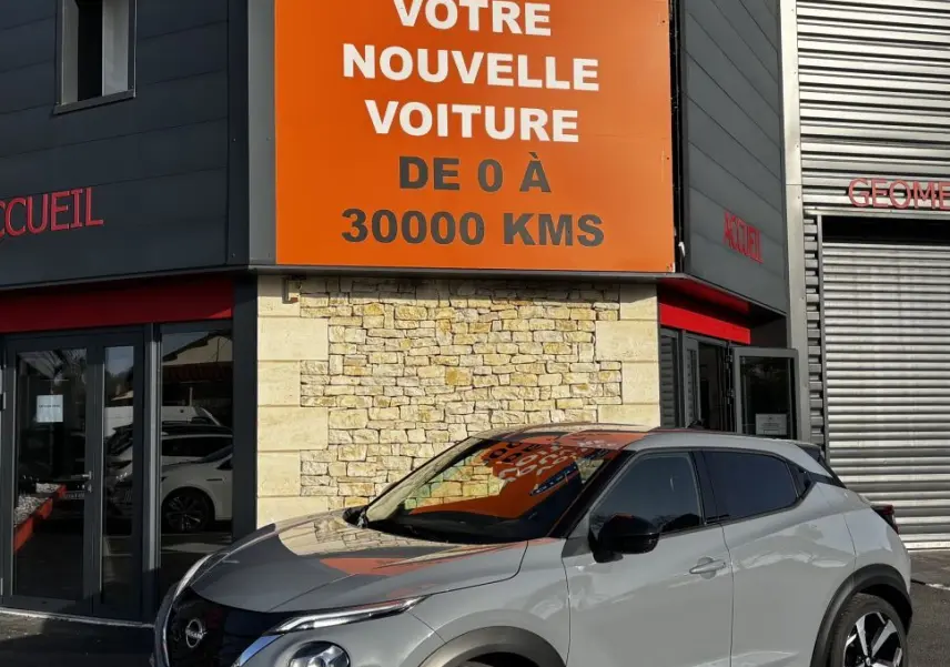 Nissan Juke Hybrid gris clair vue 3/4 avant droit, avec toit noir et jantes alliage distinctives.