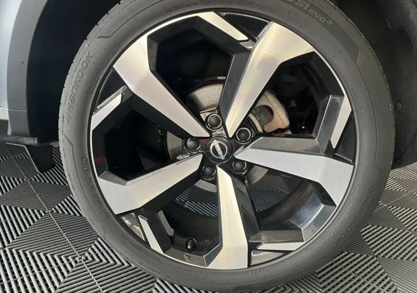 Gros plan sur la jante alliage bicolore noir et argent du Nissan Juke Hybrid 2024 gris clair, vue côté droit.