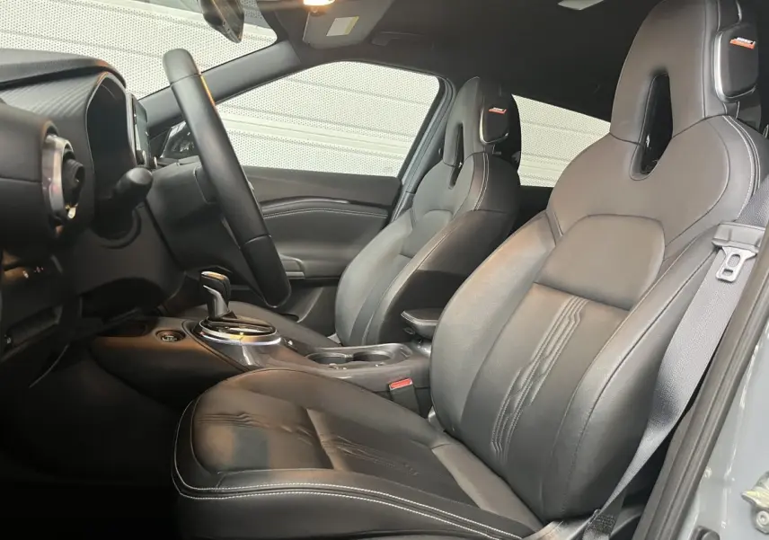 Vue intérieure côté conducteur du Nissan Juke Hybrid 143 Tekna cuir, sièges sport noirs avec surpiqûres blanches.