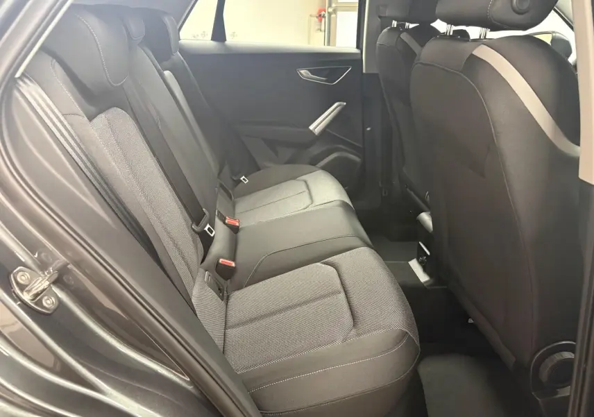 Vue intérieure de la banquette arrière de l'Audi Q2 35 TFSI S Line 2026 avec sellerie tissu gris et portes ouvertes côté gauche.