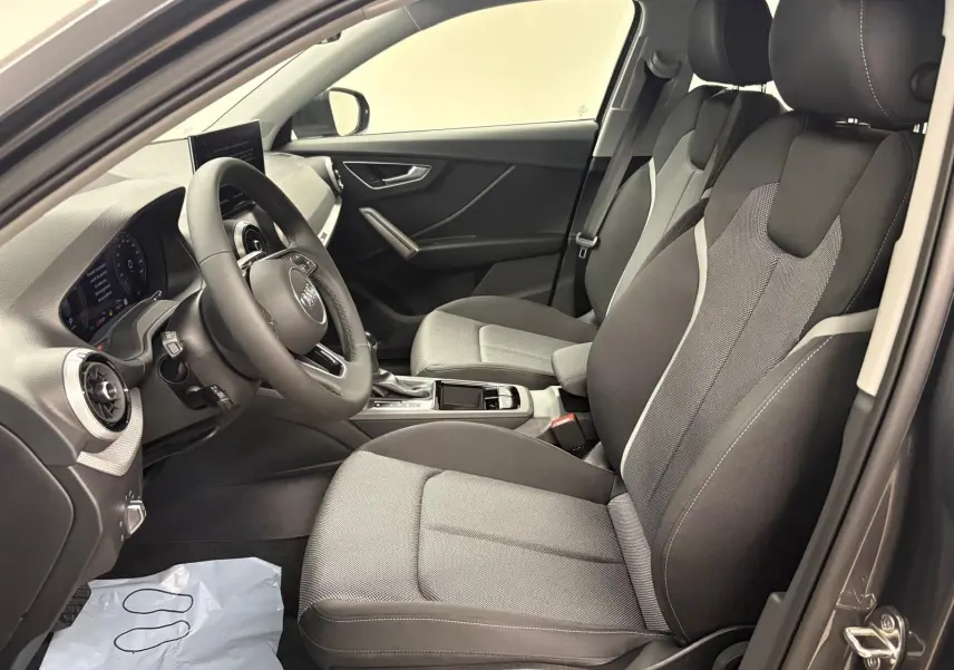 Vue intérieure côté gauche de l'Audi Q2 35 TFSI S Line 2026, sièges tissu gris et tableau de bord moderne.